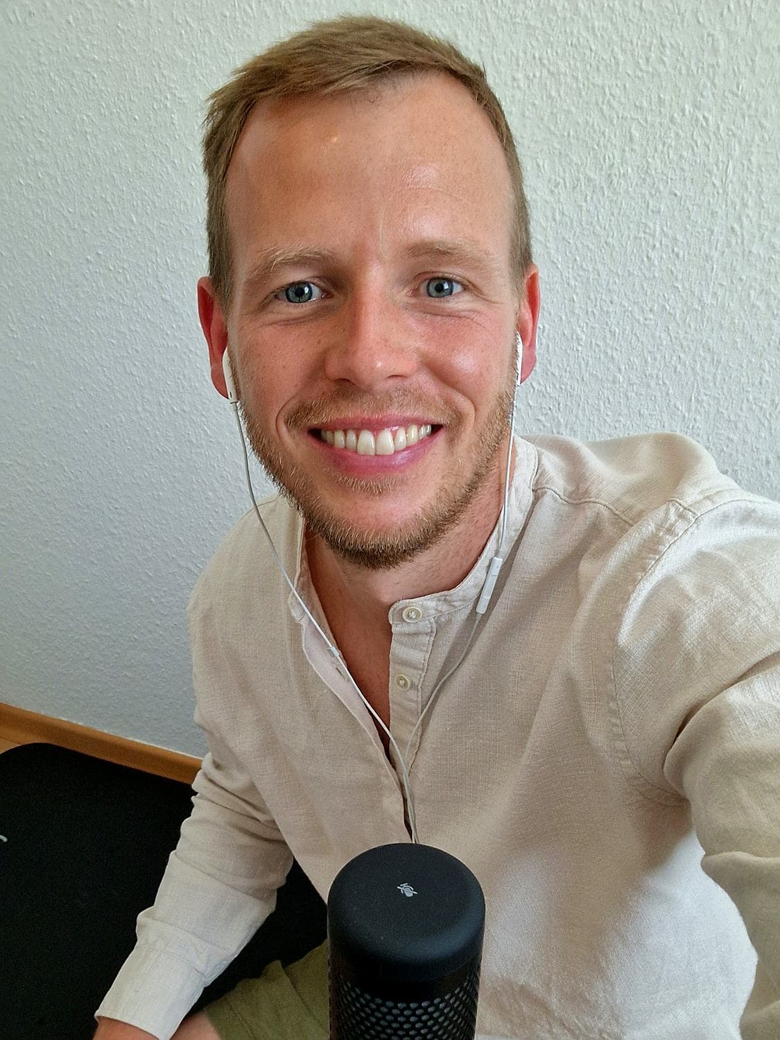 Nils Hammann lächelt mit Kopfhörern in die Kamera, das Kabel läuft über sein helles Leinenhemd