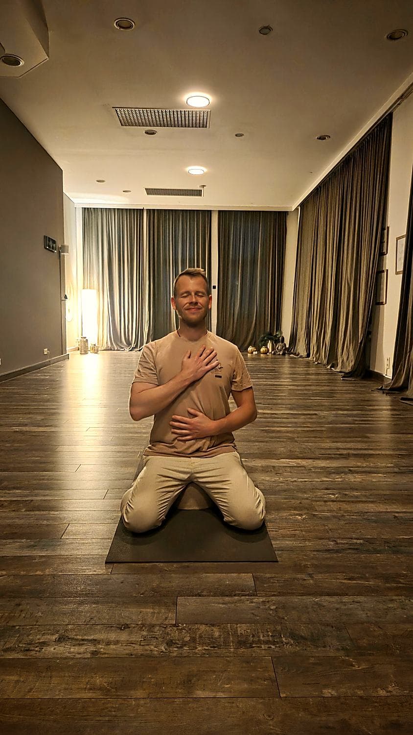 Nils Hammann kniet mit geschlossenen Augen auf einer Matte und legt eine Hand auf die Brust, die andere auf den Bauch