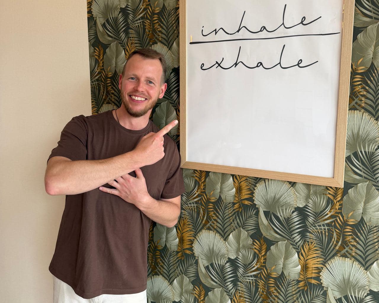 Nils Hammann zeigt lächelnd auf ein Bild mit dem Schriftzug inhale exhale
